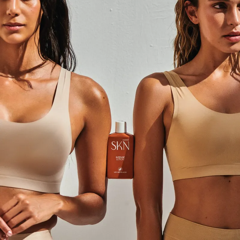 Intense lotion shot, warm orange bottle on a neutral surface.